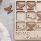 A wooden tic-tac game board with wooden tic-tac pieces shaped like whale tails, and the word "TIC-TAC-Massachusetts" written on the board.