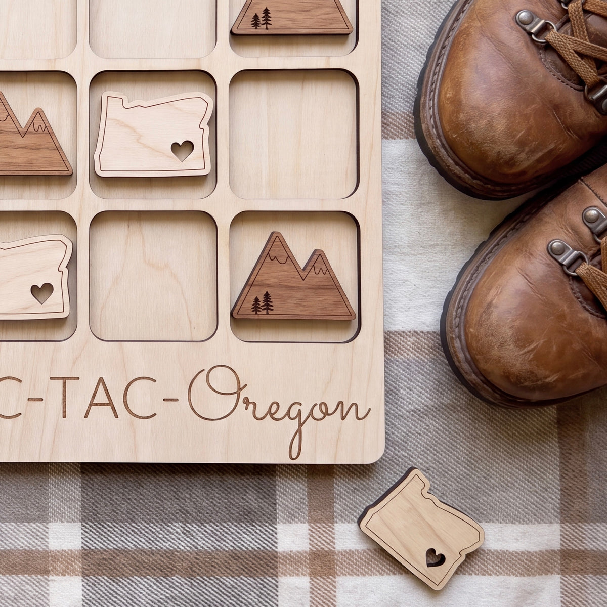 a wooden tic-tac game board with the word "Oregon" written on it, along with a pair of brown hiking boots placed next to it.