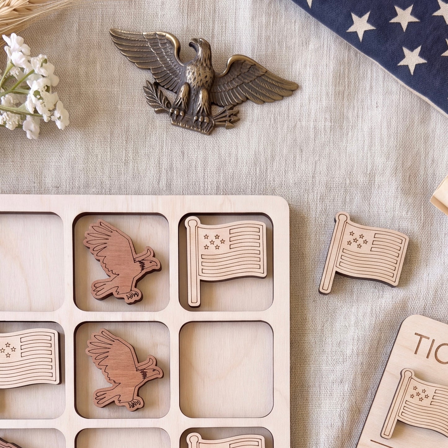 a wooden game board with wooden eagle and flag pieces, along with a blue and white flag and some flowers.