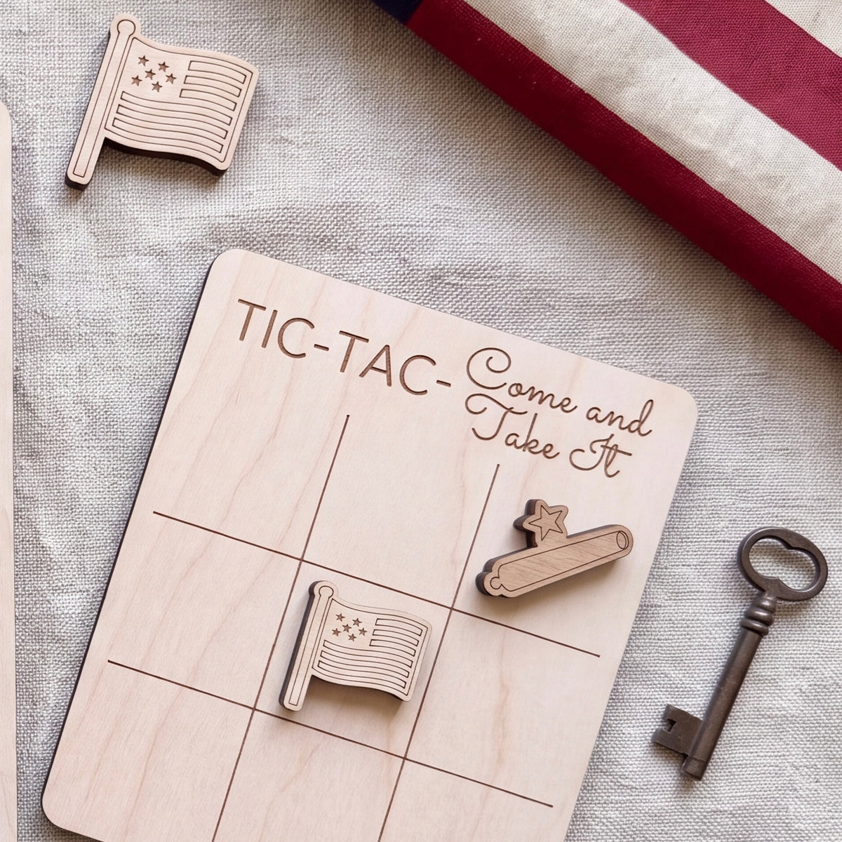 a wooden Tic-Tac game board with a key and a flag, along with a flag and a key, all placed on a grey cloth.