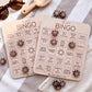 two wooden bingo cards with various beach-themed items and activities listed on them, along with some wooden bingo pieces and sunglasses on a striped towel.