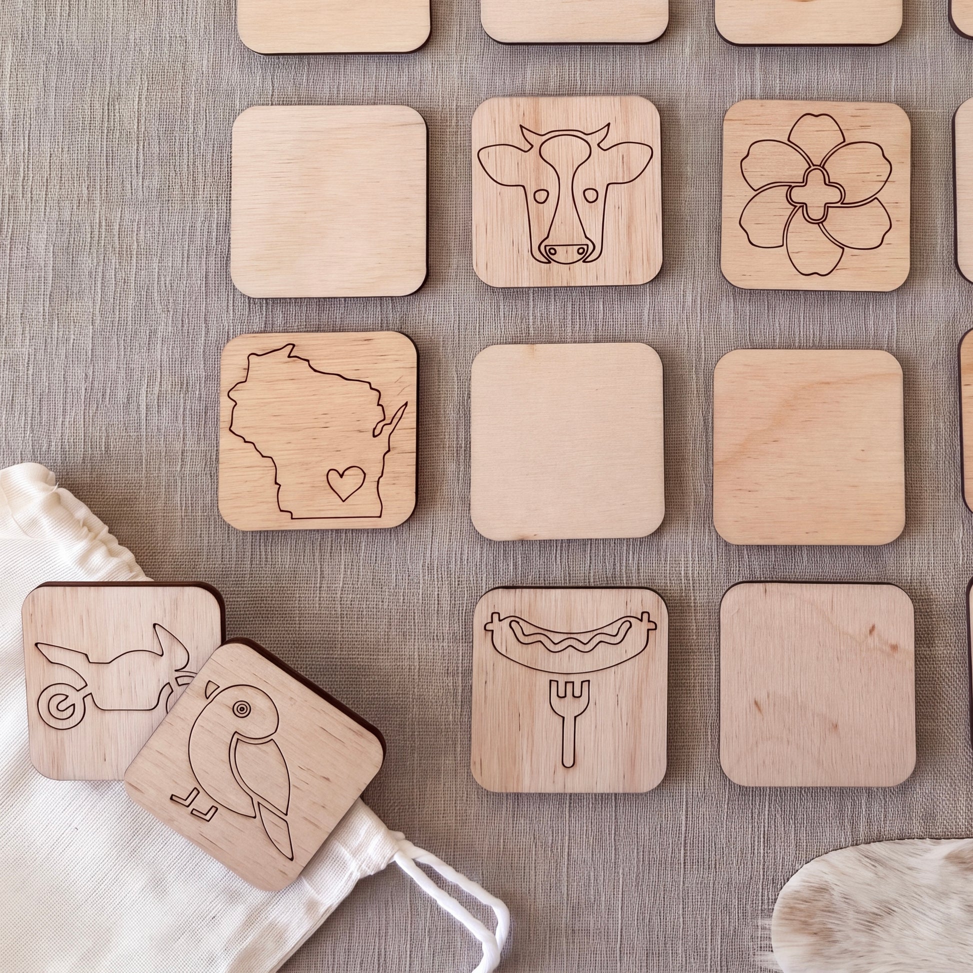 a collection of wooden coasters or game pieces with various simple designs, including a cow, flower, bird, and hot dog, arranged on a grey surface.