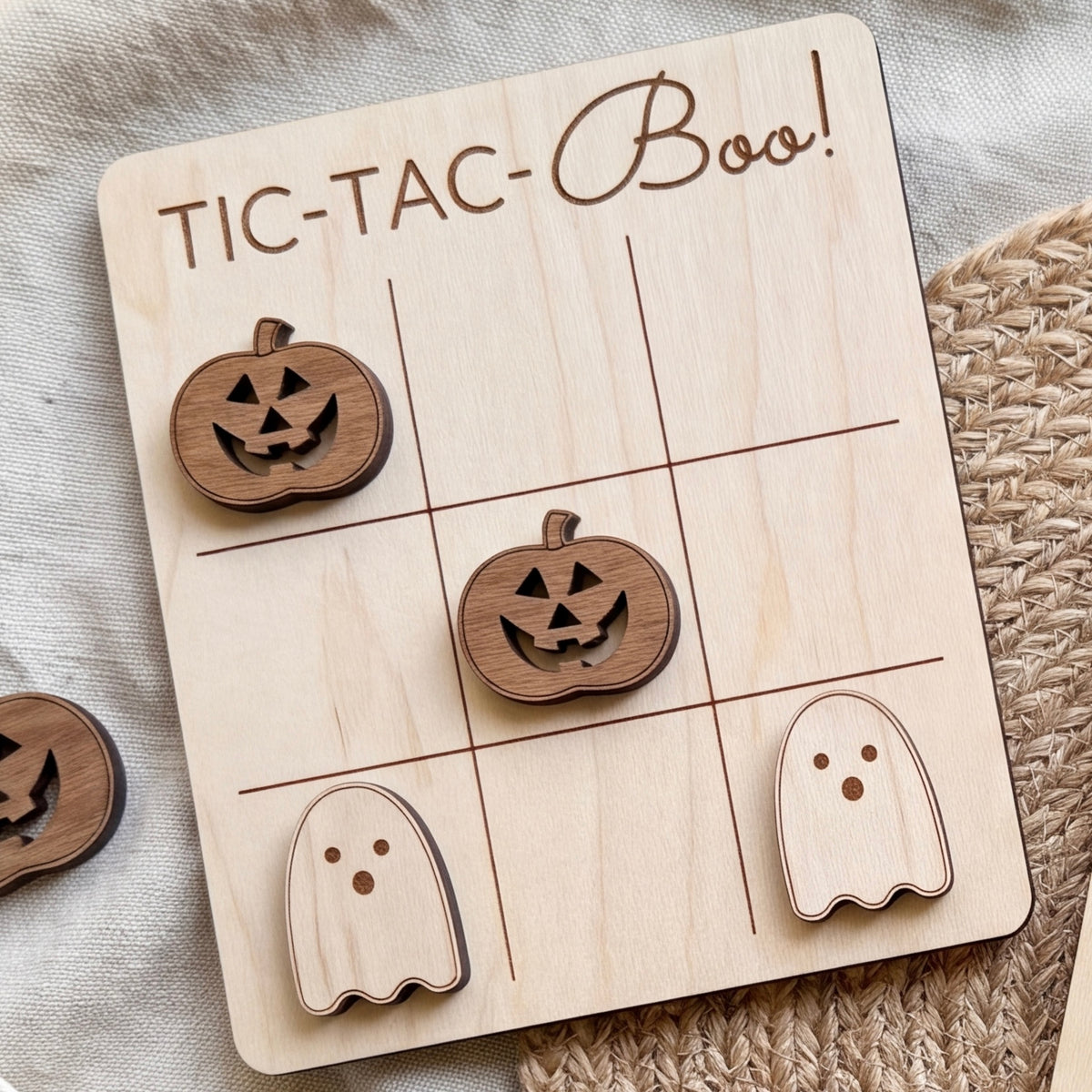 A wooden tic-tac game board with carved pumpkin and ghost pieces, along with the text "TIC-TAC-BOO!" written on the board.