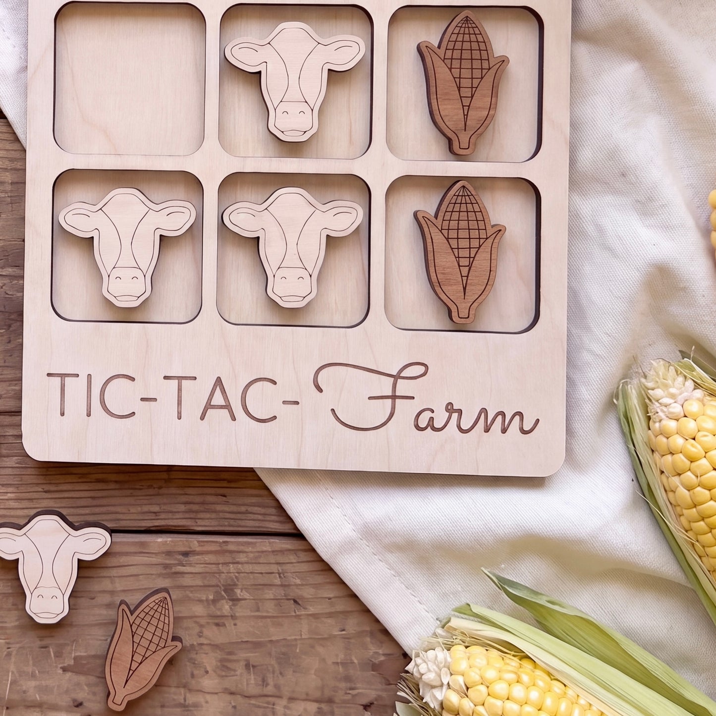a wooden game board with a farm theme, along with some corn and cow-shaped cutouts.