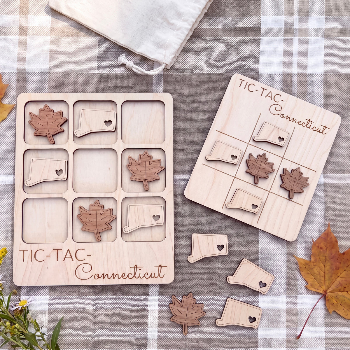 a wooden Tic-Tac Connecticut game board and several wooden leaf-shaped tiles, along with some autumn leaves on a plaid cloth.