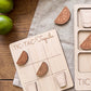 a wooden tic-tac game board with wooden cutout pieces shaped like tequila glasses and limes, placed on a wooden surface.