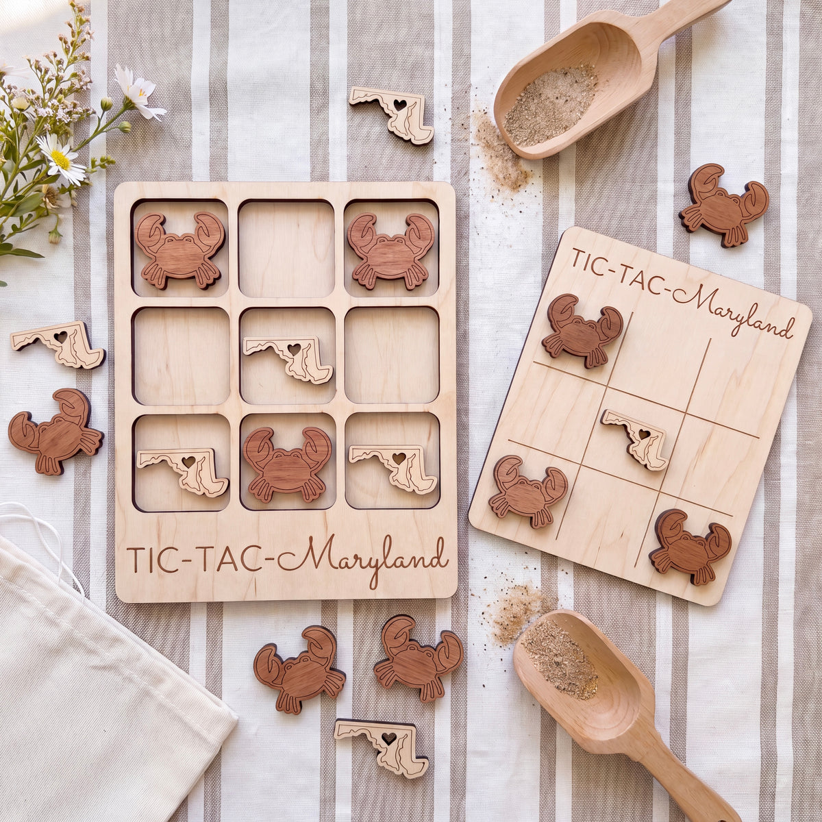 a wooden tic-tac game set with various wooden pieces, including crabs, placed on a striped cloth. There are also wooden spoons and a bag of sand nearby, suggesting the game is set up for a beach-themed game.