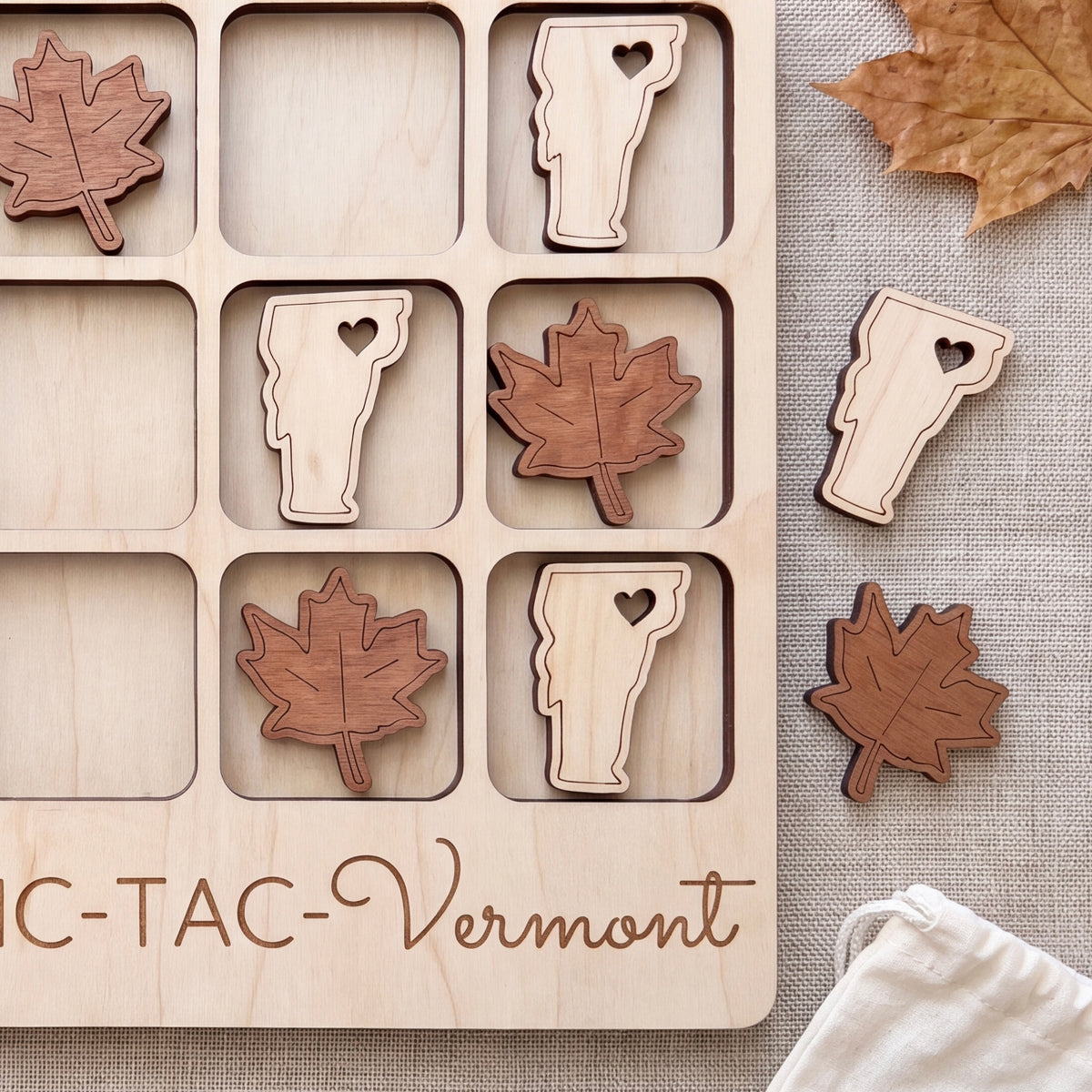 A wooden tic-tac game with wooden pieces shaped like states and leaves, including Vermont, placed on a wooden surface.