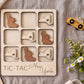 A wooden tic-tac board with various shapes cut out, including a heart-shaped piece, a wooden bear, and a wooden car, along with a toy taxi and some flowers.