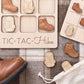 a wooden tic-tac game with wooden pieces shaped like hiking boots and a shoe, as well as a pair of brown boots on a plaid surface.