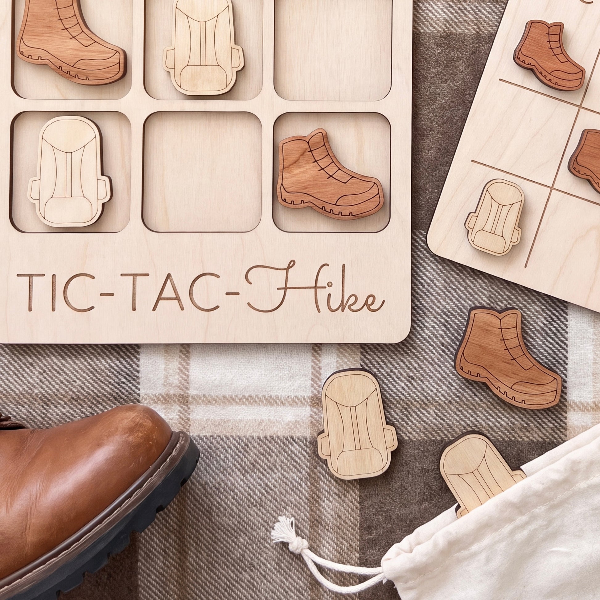a wooden tic-tac game with wooden pieces shaped like hiking boots and a shoe, as well as a pair of brown boots on a plaid surface.