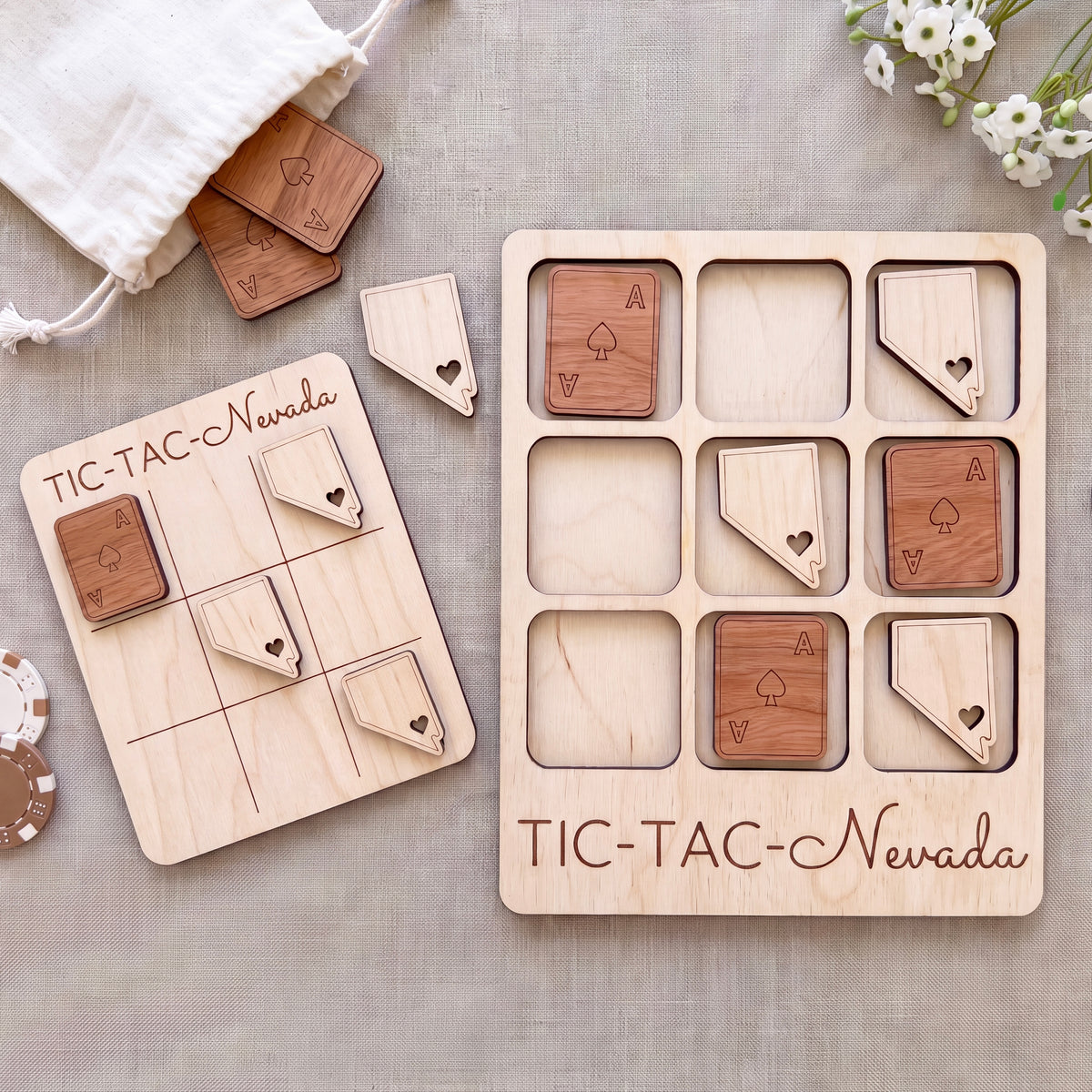 a wooden Tic-Tac- Nevada game board and game pieces, along with a white cloth and some flowers.