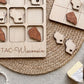 a wooden game board with a Wisconsin theme, along with several wooden pieces shaped like cheese and hearts. The game board is placed on a woven placemat, and there is a piece of cheese visible in the bottom right corner of the image.