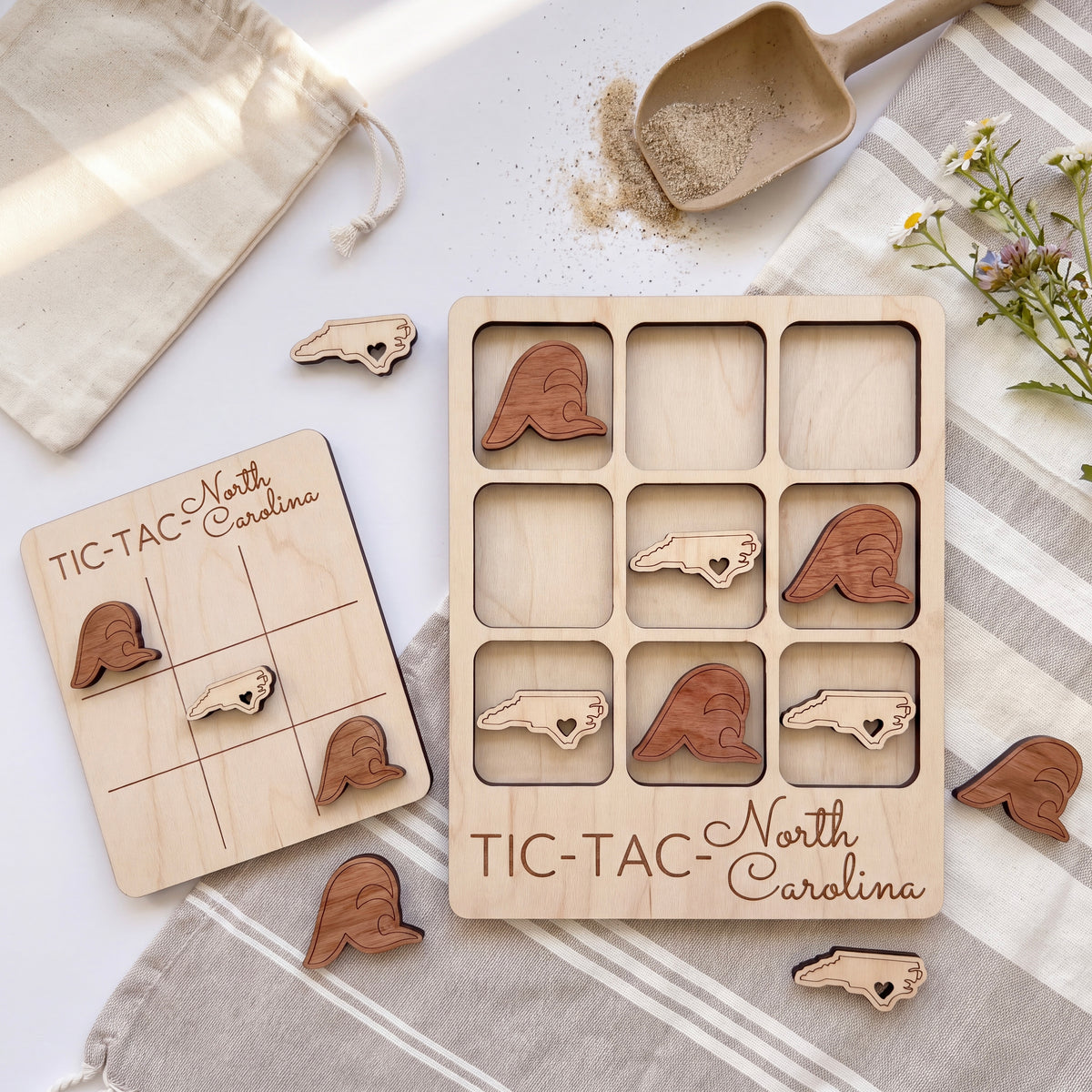 a wooden tic-tac game with the word "TIC-TAC-NORTH CAROLINA" written on it, along with several wooden pieces shaped like birds. The game is placed on a white surface, and there is a small bag and a wooden scoop nearby.