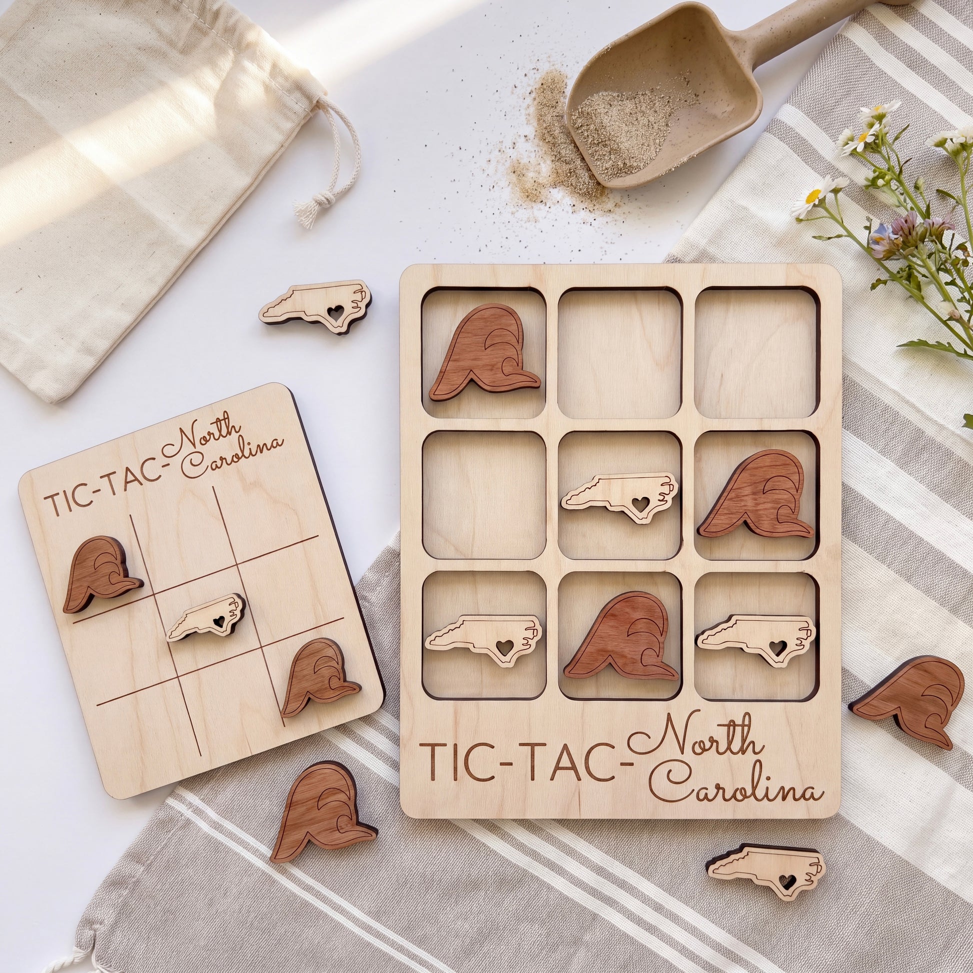 a wooden tic-tac game with the word "TIC-TAC-NORTH CAROLINA" written on it, along with several wooden pieces shaped like birds. The game is placed on a white surface, and there is a small bag and a wooden scoop nearby.