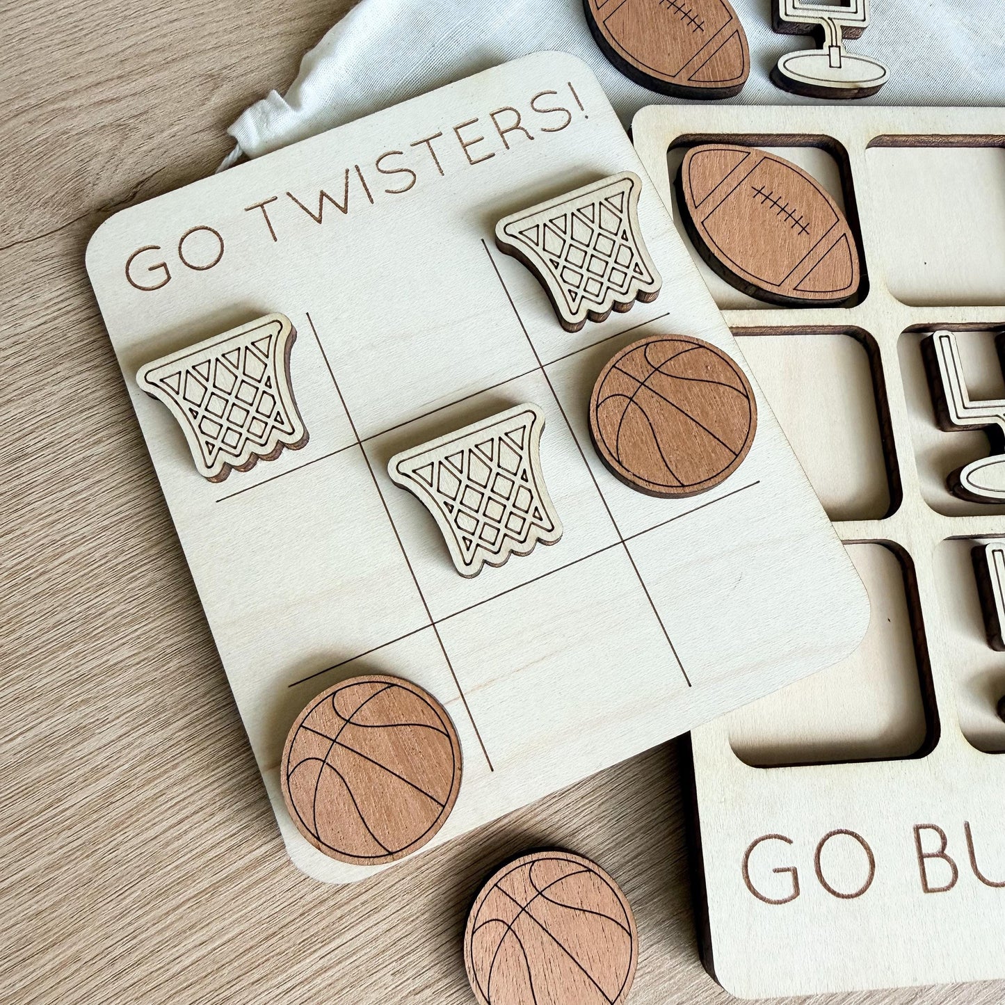 a wooden tic-tac-toe board with various sports-themed tiles, including a basketball, a football, and a tennis ball. The board also has a "GO TWISTERS!" sign on it.
