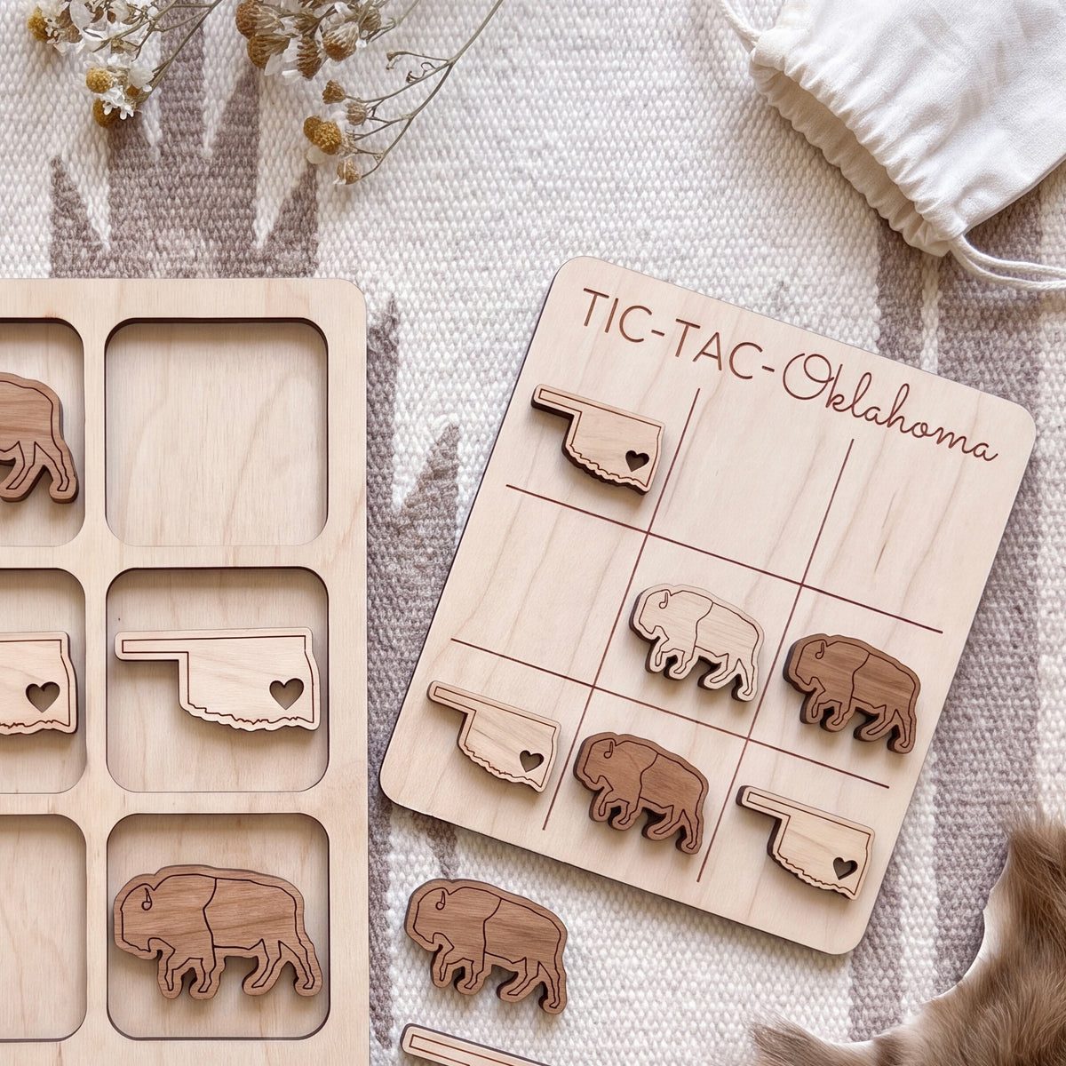 a wooden tic-tac game with a Texas state theme, including a wooden teddy bear and a wooden state flag. The game is placed on a white surface, and there is a white cloth and a small white bag in the background.