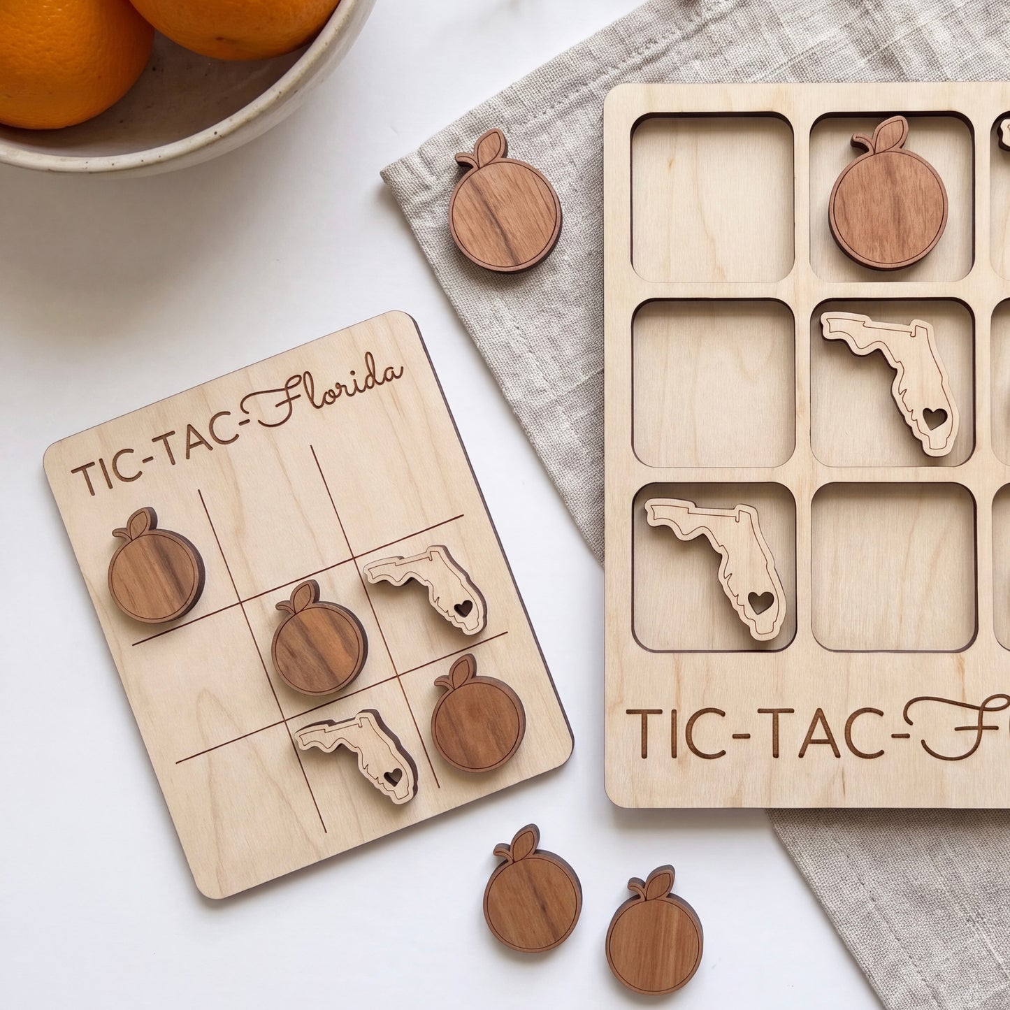 a wooden tic-tac game with wooden pieces shaped like Florida and an empty wooden board with the same design. There are also some oranges visible in the background.