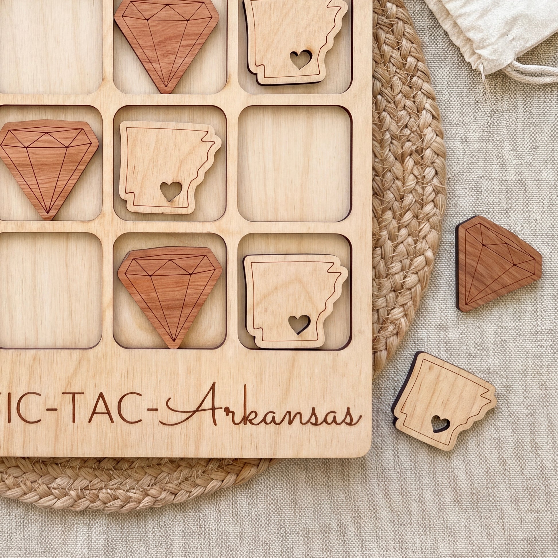 a wooden tic-tac game board with wooden pieces shaped like diamonds and hearts, and the word "ARKANSAS" written on the board.