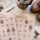 a pair of wooden bingo cards with various camping-related questions and bingo numbers, along with a lantern and some brown shoes.