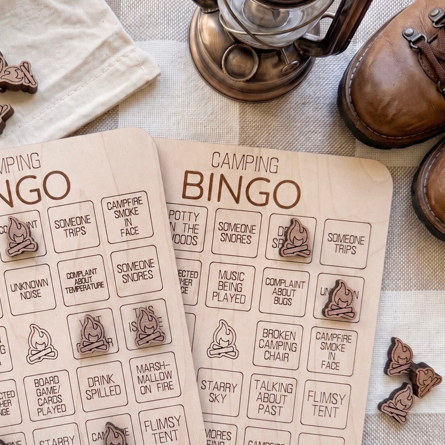 a pair of wooden bingo cards with various camping-related questions and bingo numbers, along with a lantern and some brown shoes.