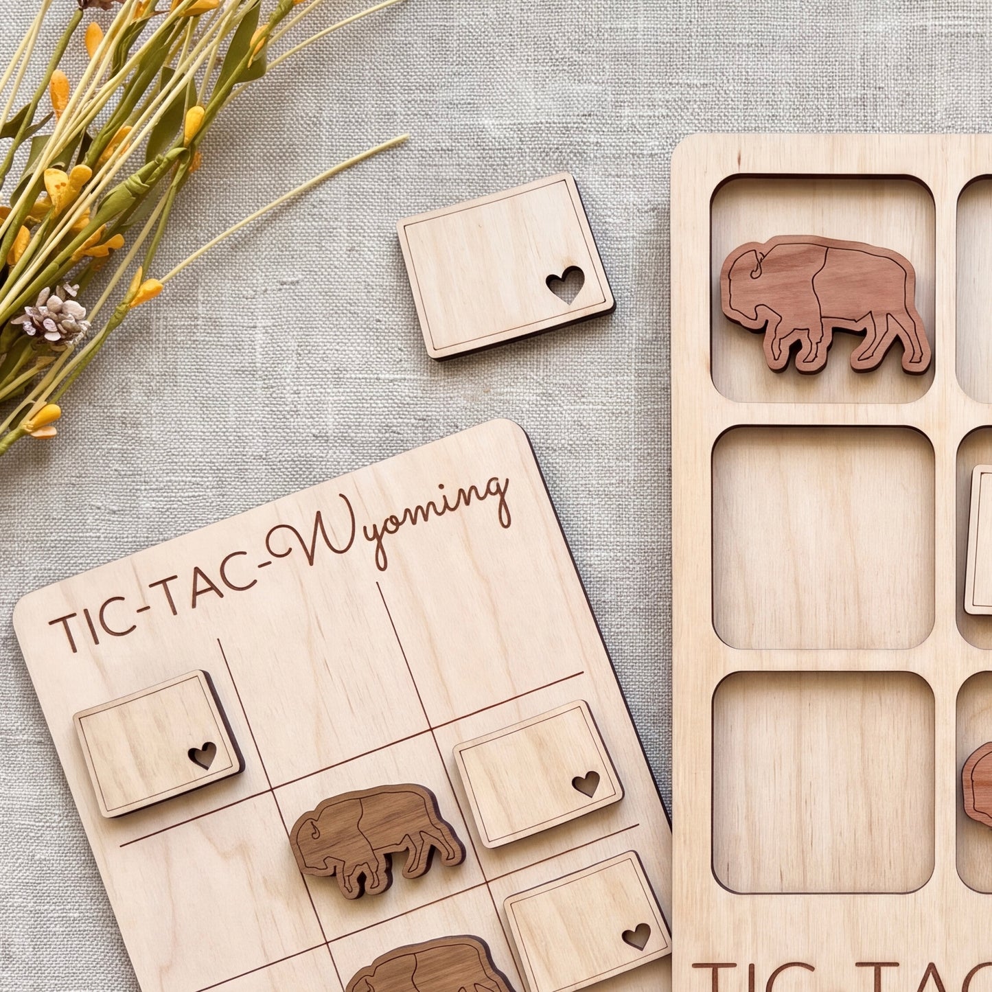 a wooden Tic-Tac-To-Win-Dix board game with wooden pieces shaped like buffalo and a wooden card with a heart cutout.