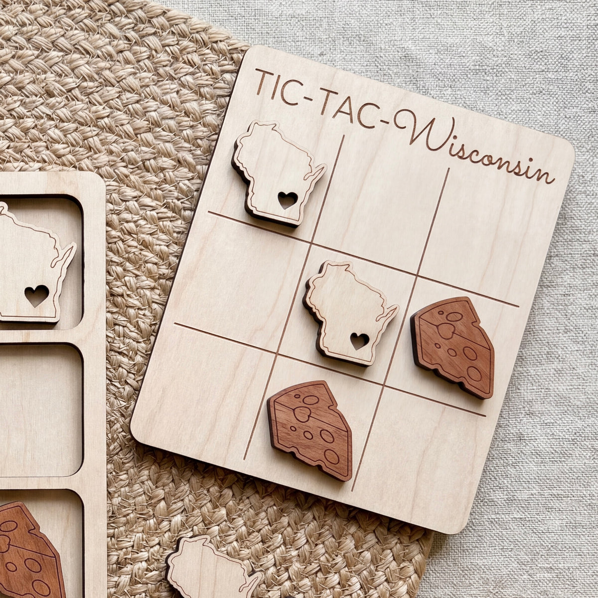 A wooden tic-tac game board with a Wisconsin state map and cheese pieces on it, placed on a woven surface.