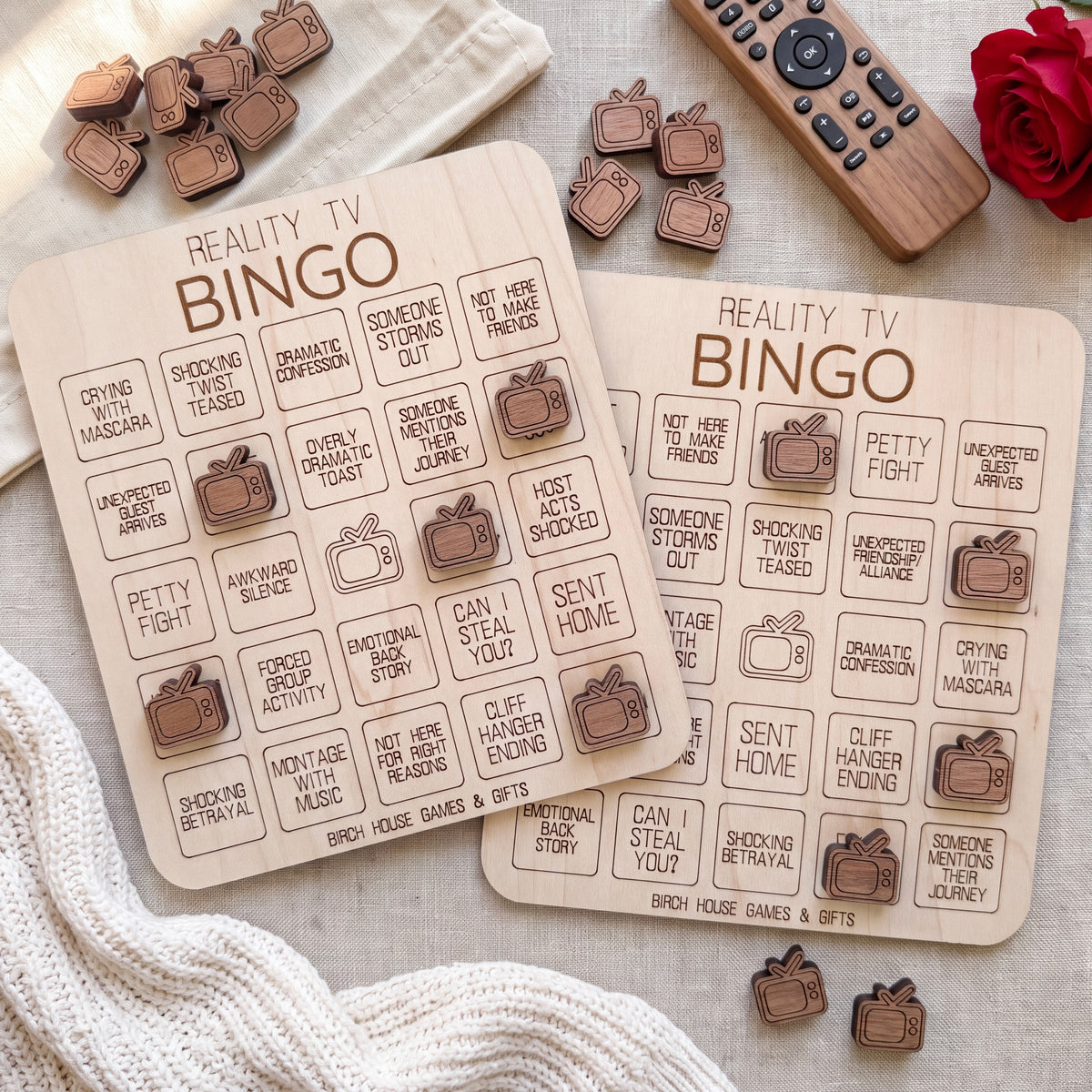 two wooden bingo cards with various TV-related questions and bingo squares, along with several wooden bingo pieces and a remote control on a beige surface.