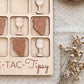 a wooden tic-tac game board with wooden pieces shaped like wine glasses and grapes, placed on a beige cloth.