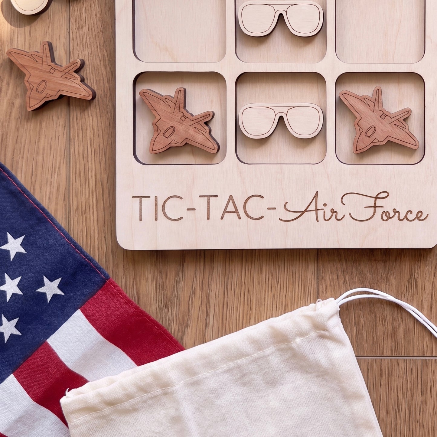 a wooden tic-tac game with a wooden airplane and a wooden pair of sunglasses on it, along with a white cloth and a red and white American flag.