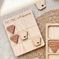 a wooden tic-tac game board with wooden pieces shaped like diamonds and hearts, placed on a woven placemat.
