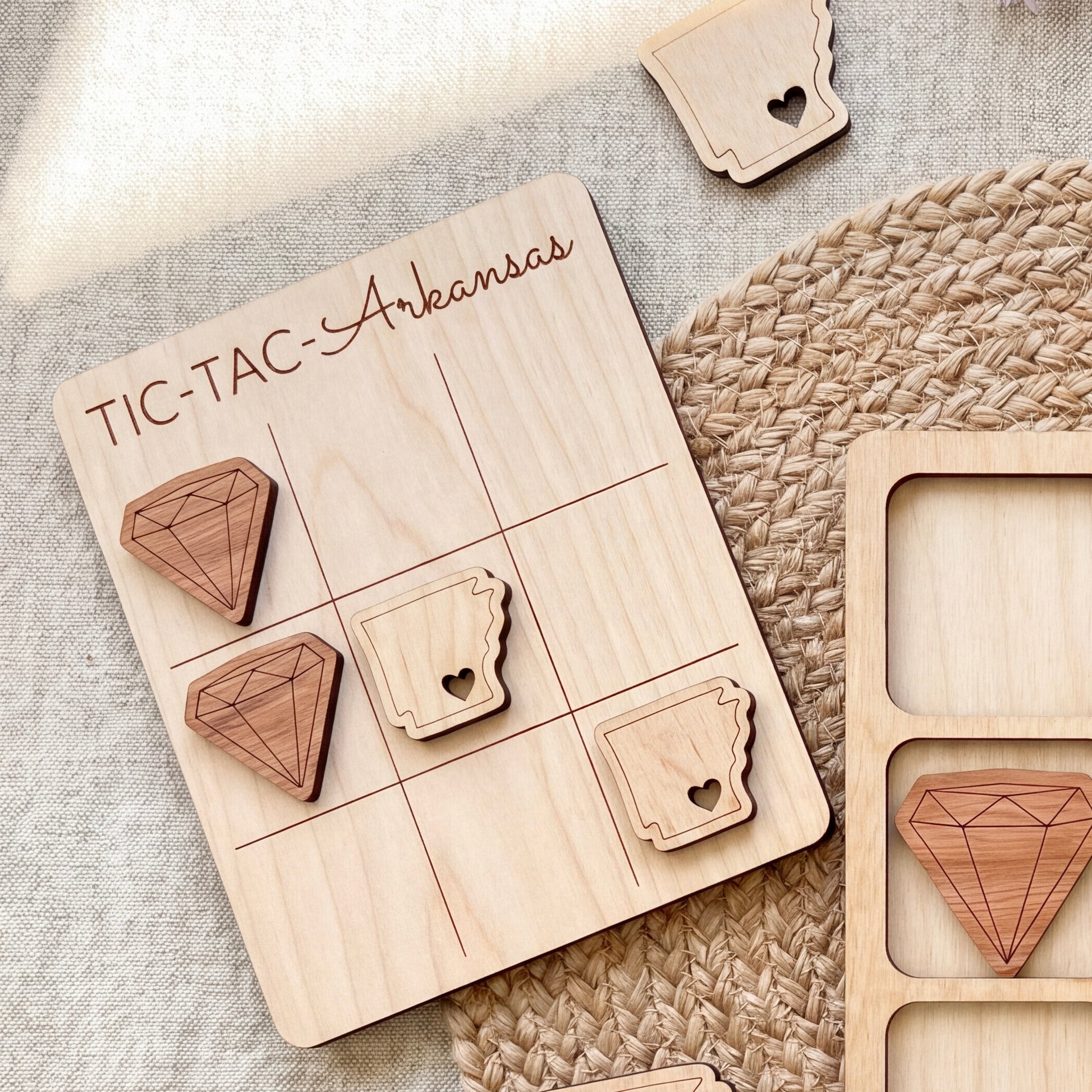 a wooden tic-tac game board with wooden pieces shaped like diamonds and hearts, placed on a woven placemat.
