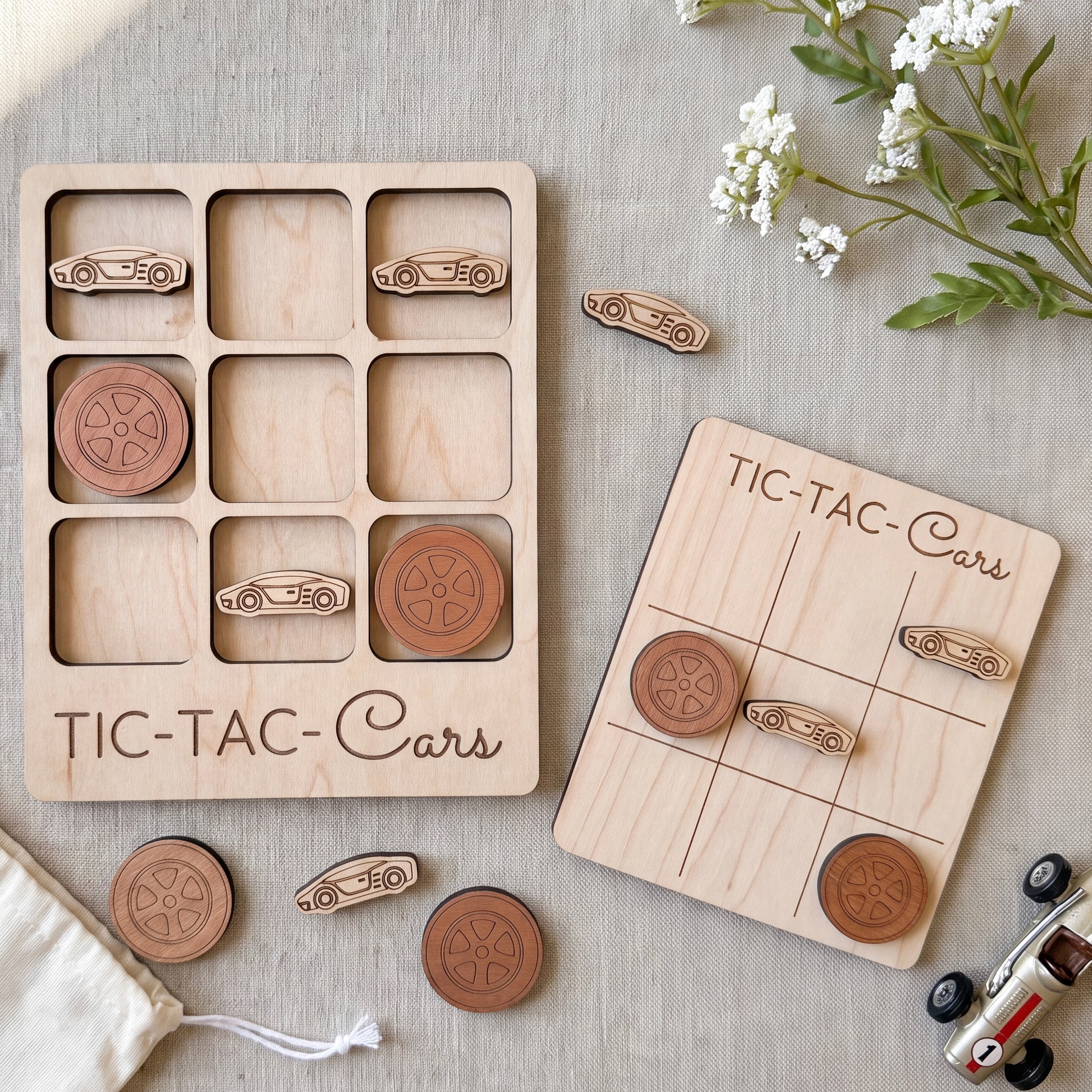 a wooden tic-tac game set with car-shaped tiles and a wooden board labeled "TIC-TAC-Cars". The game appears to be made of wood and is placed on a table with some flowers and a toy car.