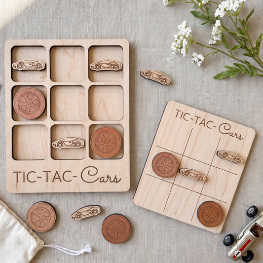 a wooden tic-tac game set with car-shaped tiles and a wooden board labeled "TIC-TAC-Cars". The game appears to be made of wood and is placed on a table with some flowers and a toy car.