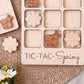 a wooden tic-tac game board with wooden pieces shaped like flowers and a wooden bee. The game board is labeled "TIC-TAC-Spring".