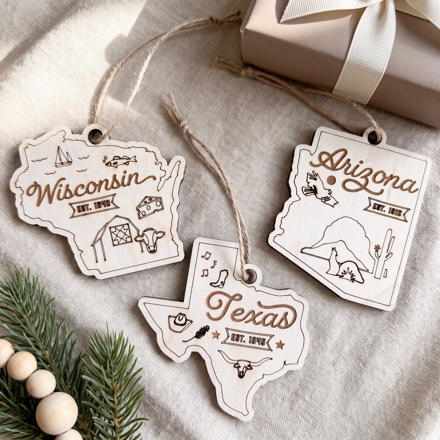 three wooden ornaments shaped like the states of Wisconsin, Arizona, and Texas, each with unique designs and text.
