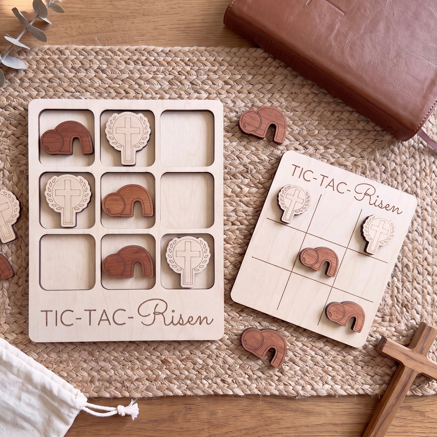 a wooden tic-tac game with wooden pieces and a wooden cross, along with a leather-bound book and a cross.