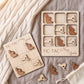 a wooden tic-tac game board and wooden tic-tac pieces, both labeled "TIC-TAC New York". The tic-tac pieces are arranged on the board, and there is a white cloth or blanket in the background.