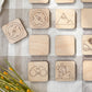 a collection of wooden shapes, including a compass, a mountain, a pair of binoculars, and a hiker, arranged on a checkered surface.
