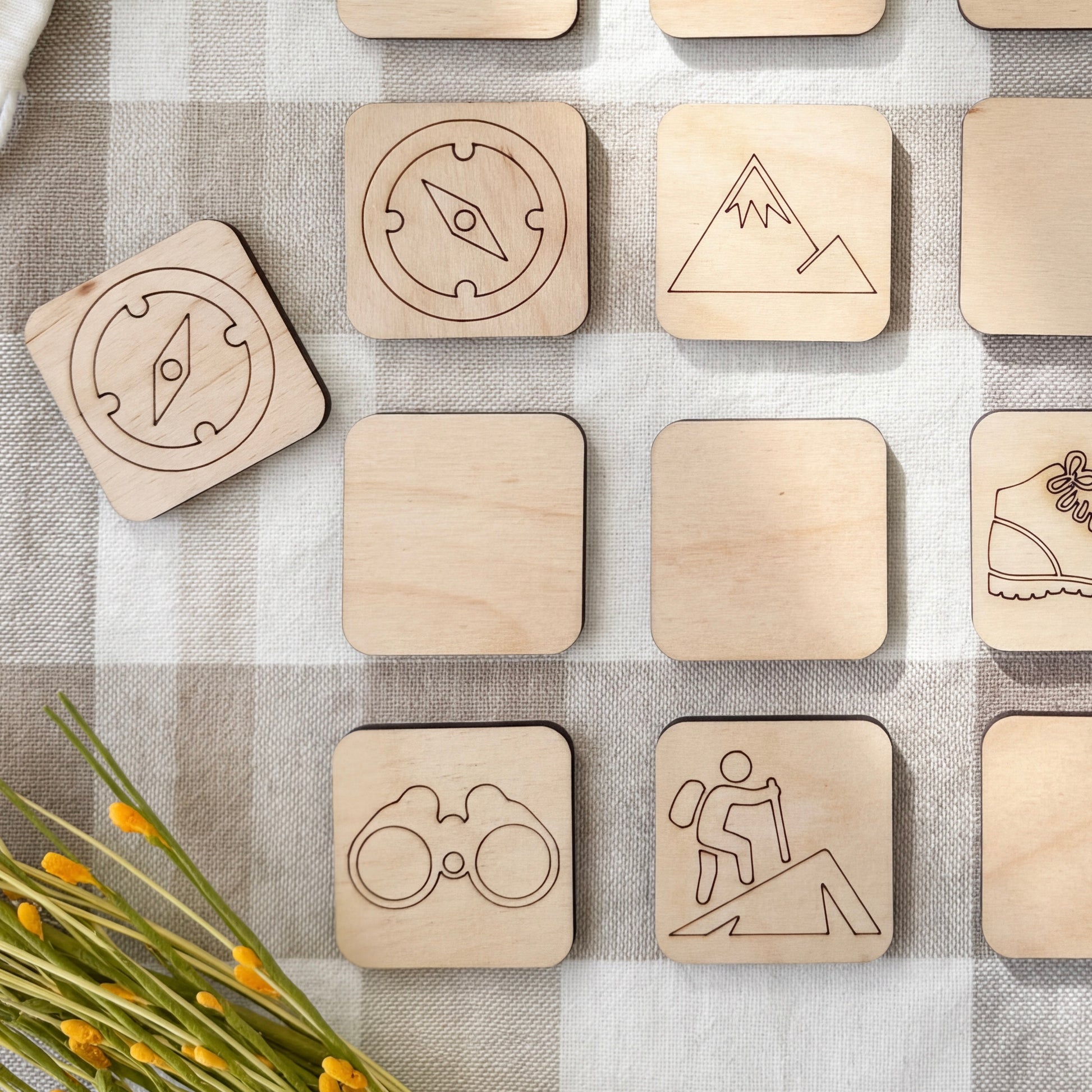 a collection of wooden shapes, including a compass, a mountain, a pair of binoculars, and a hiker, arranged on a checkered surface.