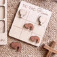 a wooden tic-tac game board with wooden pieces, including a cross and a heart, arranged on a woven surface.