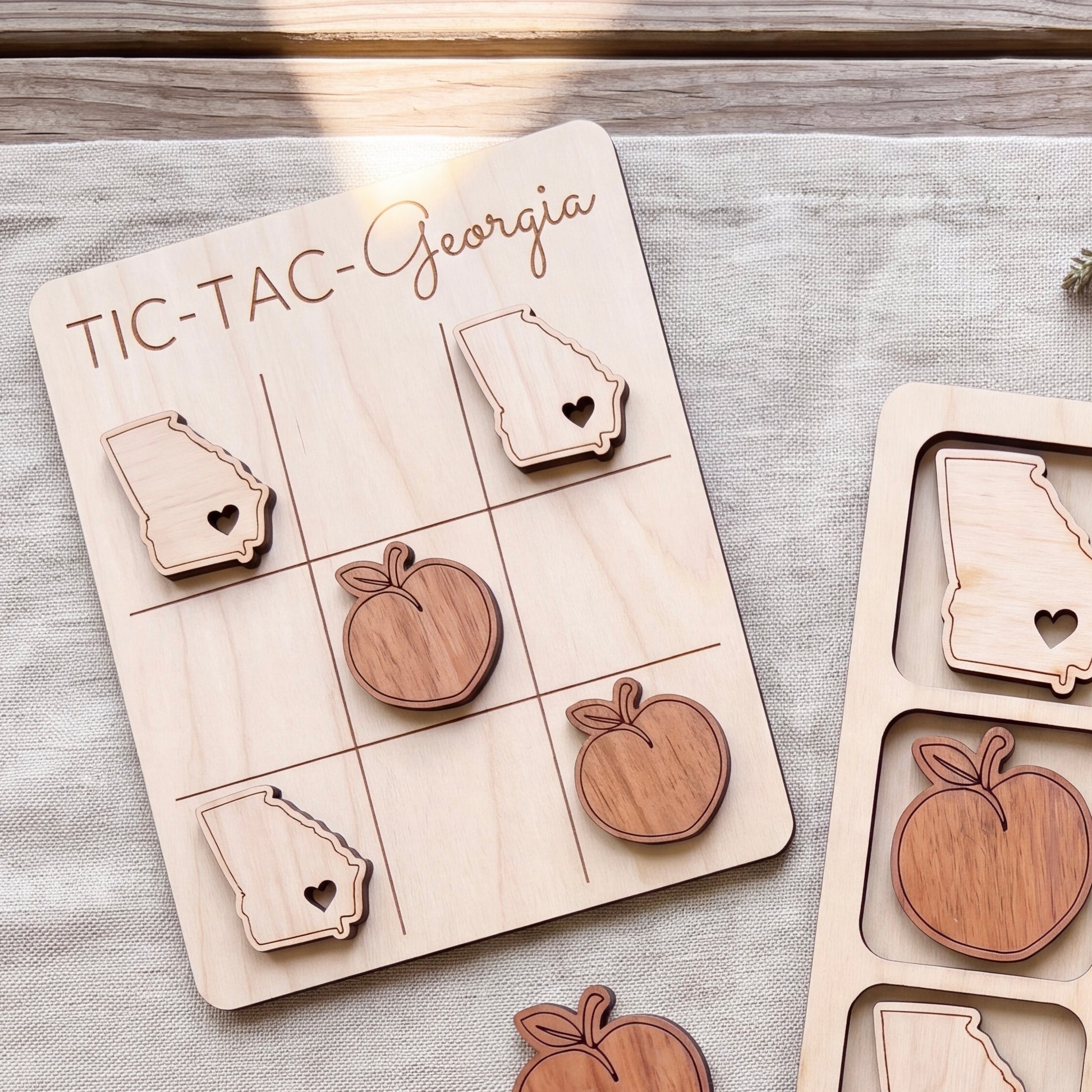 A wooden tic-tac game board with wooden pieces shaped like the states of Georgia, including a peach and an apple.