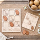 a wooden tic-tac game with Idaho potato pieces, a bowl of potatoes, and some flowers on a woven placemat.