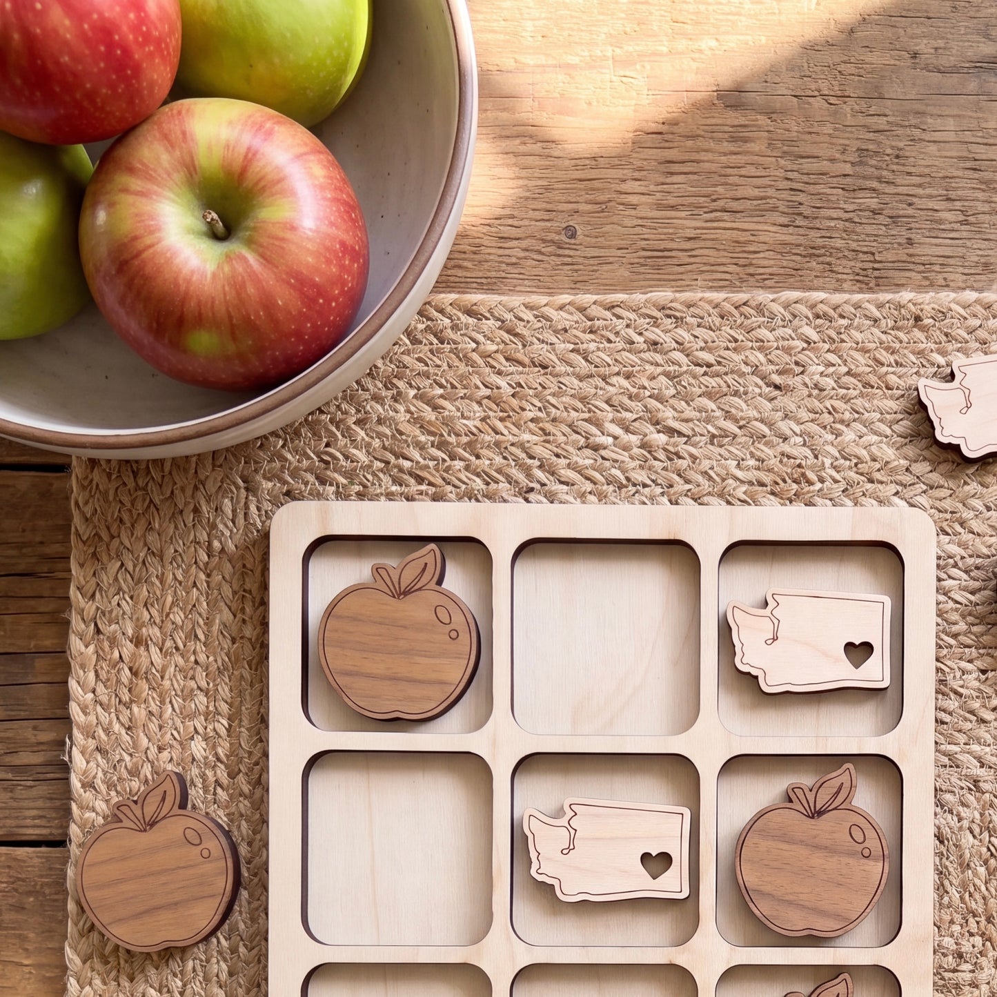 a wooden teddy bear with a heart on it, placed on a woven placemat next to a bowl of apples.