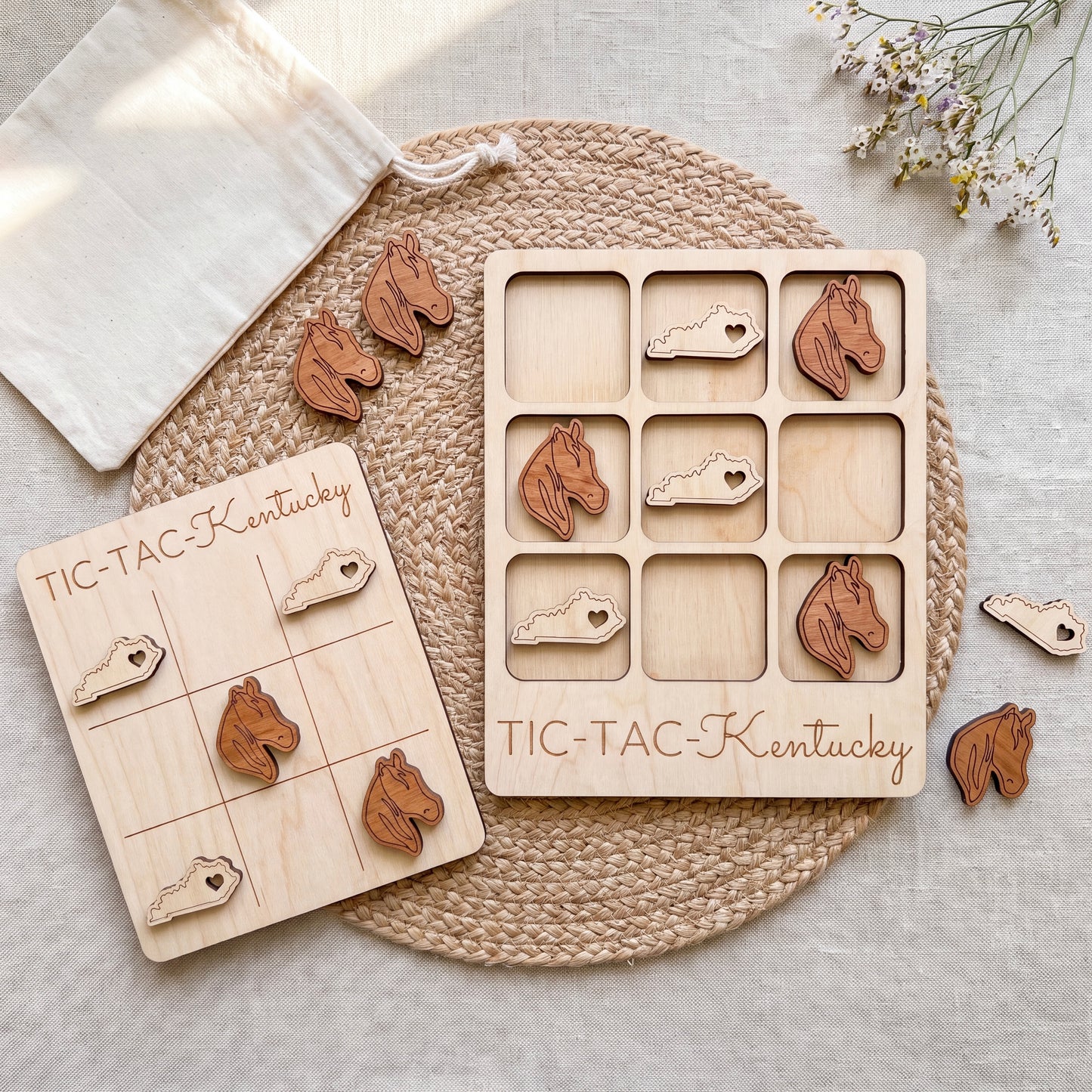 a wooden Tic-Tac-Kentucky game set, including a game board and wooden pieces shaped like horses. The game board is placed on a woven placemat, and there are some wooden pieces scattered around the board.