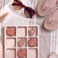 A wooden tic-tac-toe board with wooden tiles, a pair of sunglasses, and a pair of flip-flops on a striped towel.
