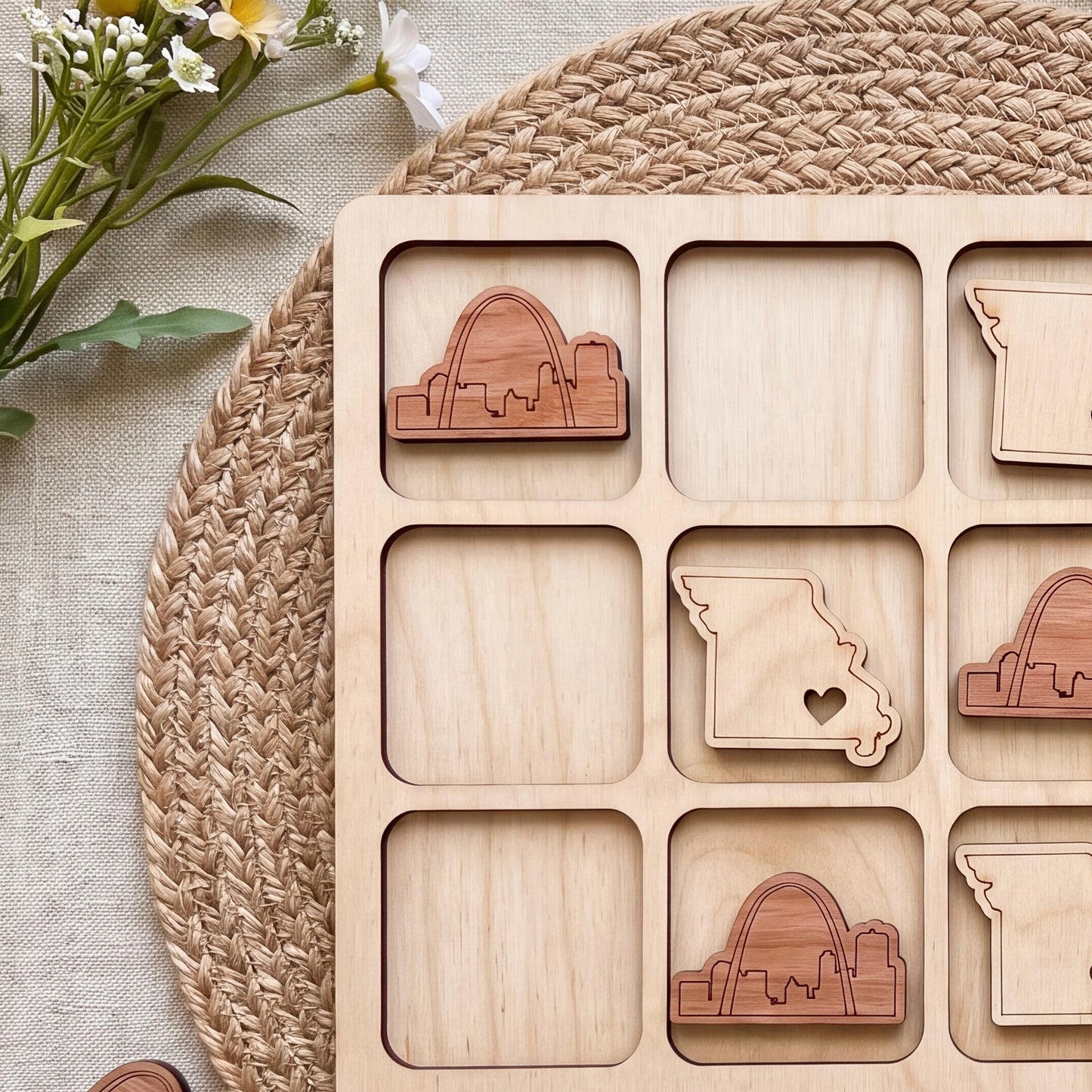 a wooden puzzle with nine pieces, each depicting a different state in the United States. The puzzle is placed on a woven placemat, and there are some flowers visible in the background.