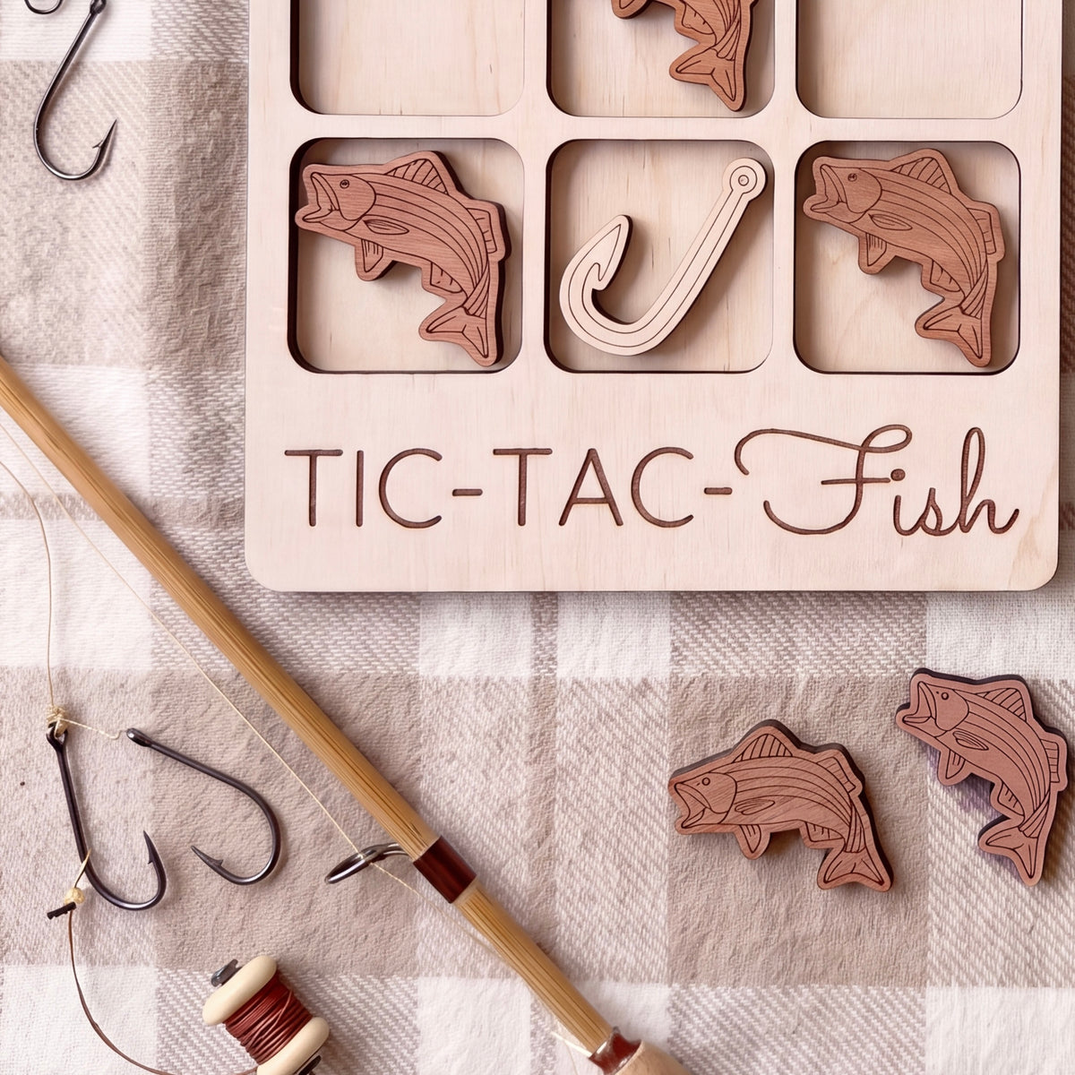 a wooden tic-tac game with fish-shaped tiles, a fishing rod, and some hooks, all arranged on a checkered cloth.