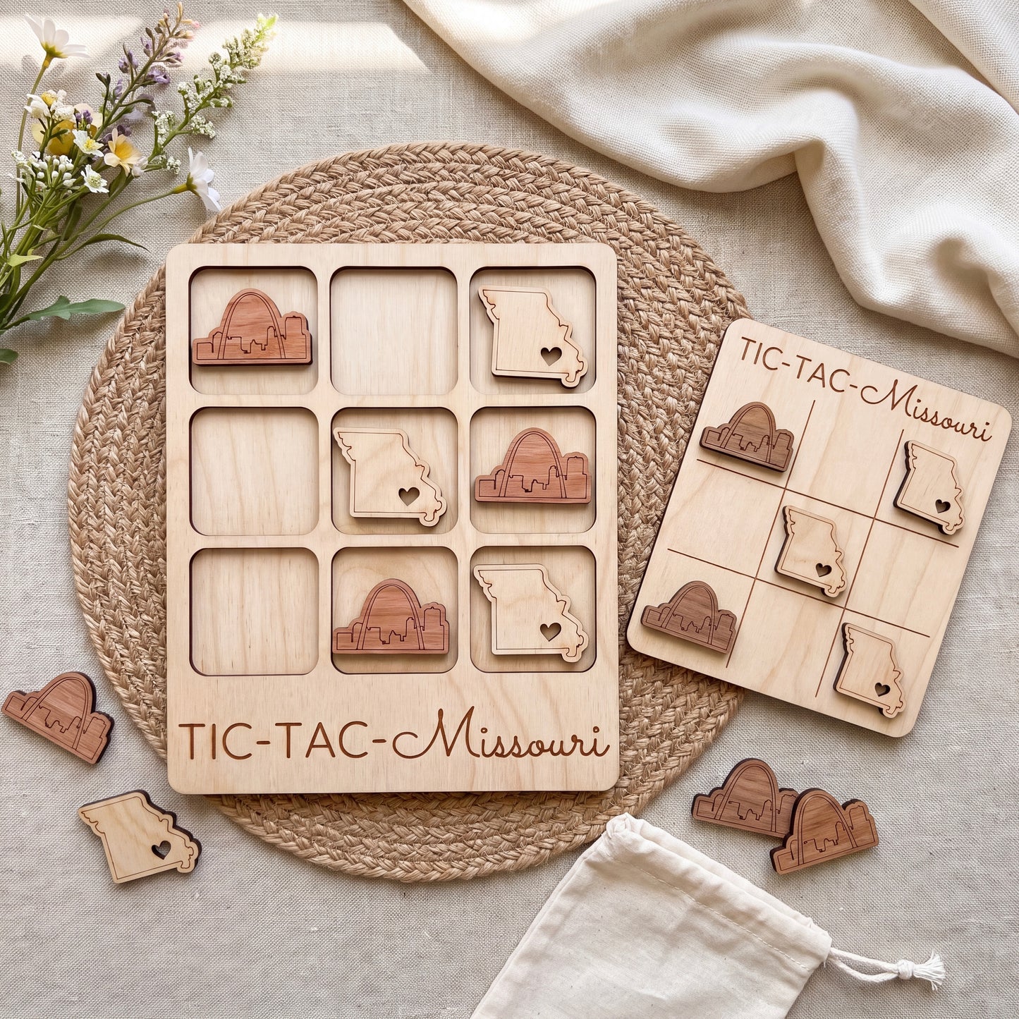 a wooden tic-tac game set with wooden pieces shaped like states, including one shaped like Missouri. The game is placed on a woven placemat, and there are some additional wooden pieces scattered around the game.
