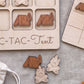 a wooden game board with a tic-tac game design, along with several wooden game pieces depicting camping scenes.